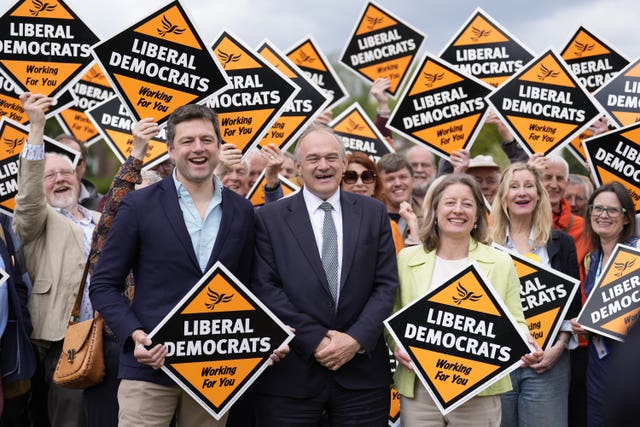 Sir Ed Davey smiling while standing at the front of a large group of Lib Dem supporters, many holding Lib Dem placards