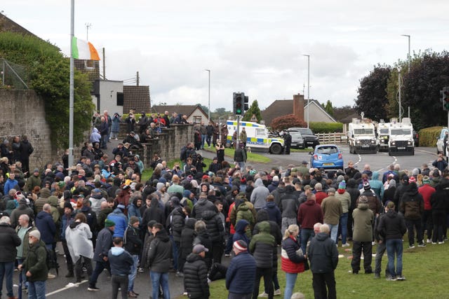A large group of protesters on a road, with police vehicles in the background