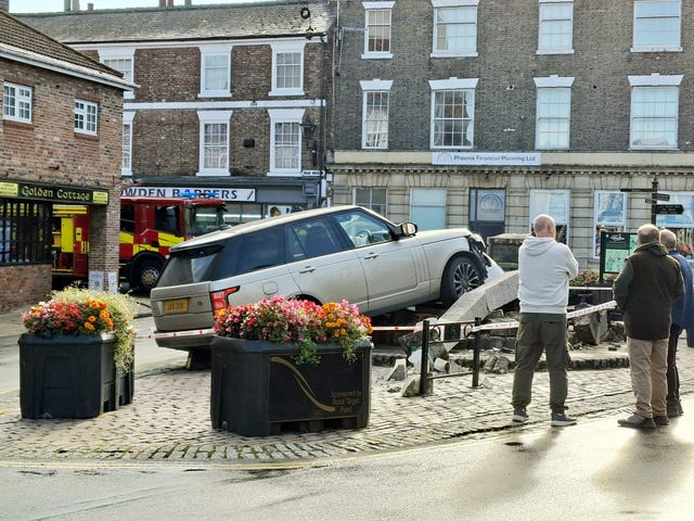 Locals examine the scene after a Range Rover mounted a paved area and knocked down the Market Cross in Howden