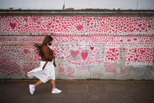 A woman walks past the National Covid Memorial Wall on the Embankment in London (Yui Mok/PA)