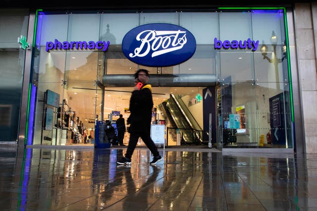 A woman on a phone walks past a branch of Boots