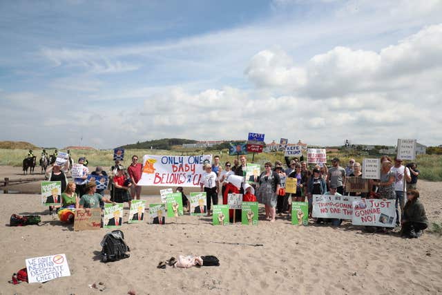 Crowds protest on a beach near the course