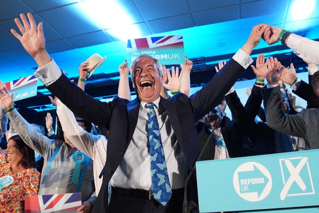 Nigel Farage beaming with his hands raised in the air as he celebrates with Reform UK campaigners