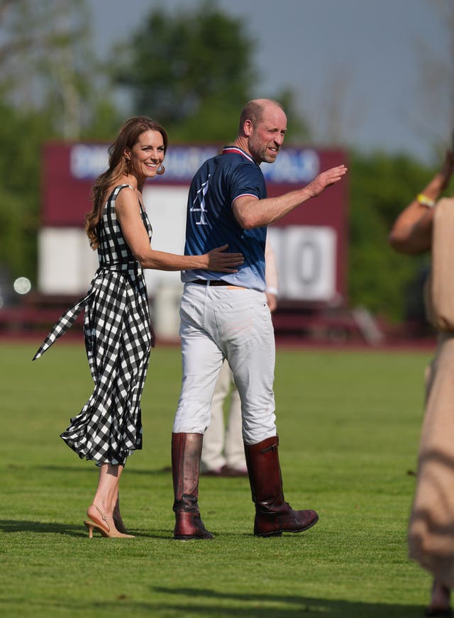 Kate places her hand on William's back and smiles while the sweaty prince turns and gestures to someone off camera