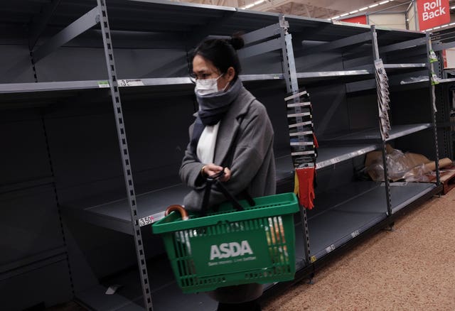 A shopper wearing a face mask walks past empty shelves as toilet roll is sold out, in an Asda store in London (Yui Mok/PA)