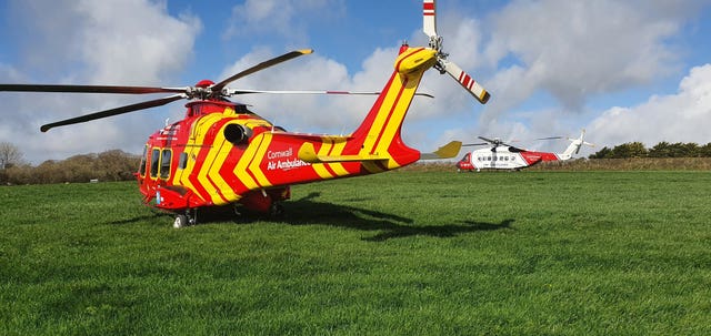 A Cornwall Air Ambulance helicopter (left) alongside a Coastguard SAR helicopter in a field adjacent to where a Royal Navy Hawk jet crashed in woodland in Cornwall after the two pilots ejected