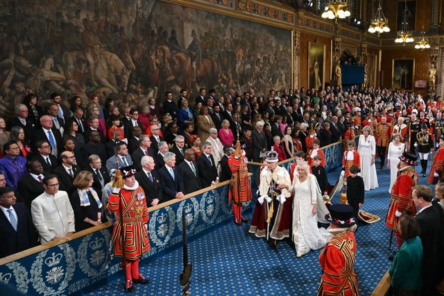 The King, wearing the Imperial State Crown and the Robe of State, and the Queen, wearing the George IV State Diadem, process through the Royal Gallery
