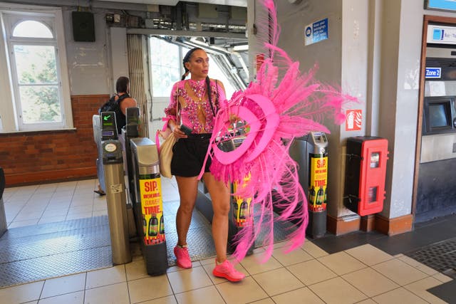 A woman in a pink costume holding a feathered headdress walks through the gates at a Tube station ahead of the Notting Hill Carnival 2025