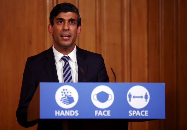 Rishi Sunak speaking during a Covid briefing, standing at a lectern with a sign on it which reads 'Heads, face, space'