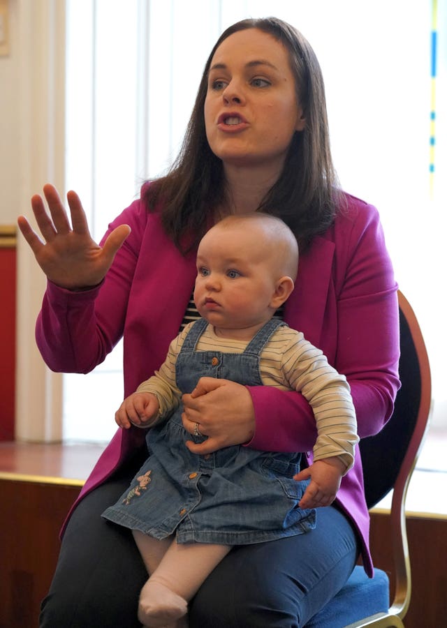 Kate Forbes speaking with her young daughter Naomi on her lap