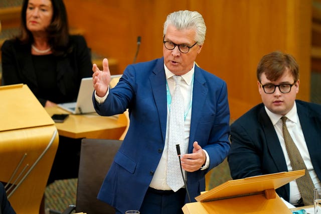 Malcolm Offord with one arm raised while speaking in Holyrood