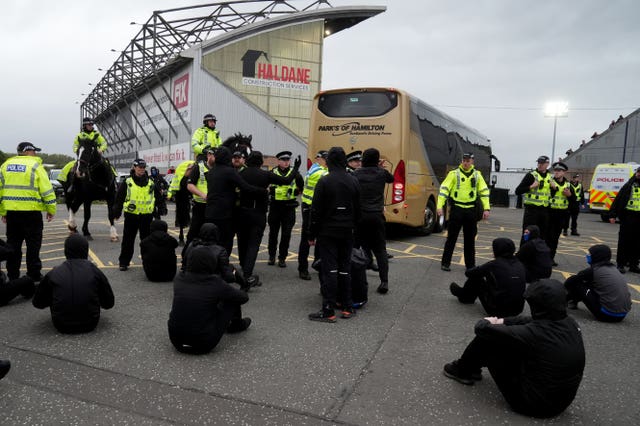 Police officers look on as Rangers fans are sat in the car park