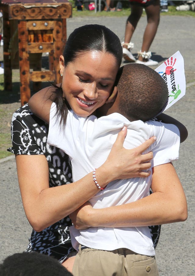 The Duchess of Sussex hugs a young child as she begins her visit to South Africa, with her husband the Duke of Sussex, in the Nyanga Township, Cape Town, during a visit to a workshop that teaches children about their rights, self-awareness and safety and which provides self-defence classes and female empowerment training to young girls in the community