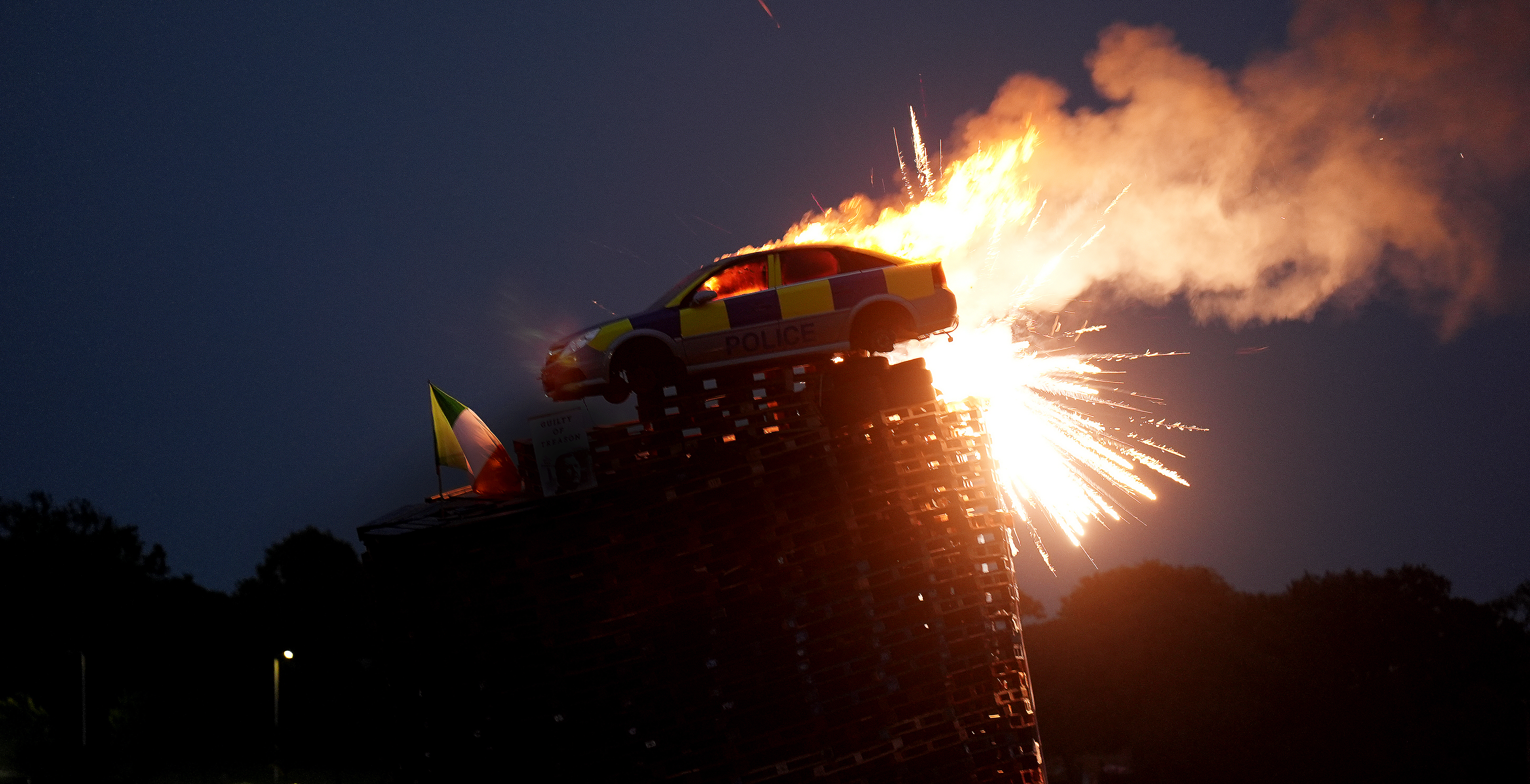 A mock police car is set alight on top of a bonfire