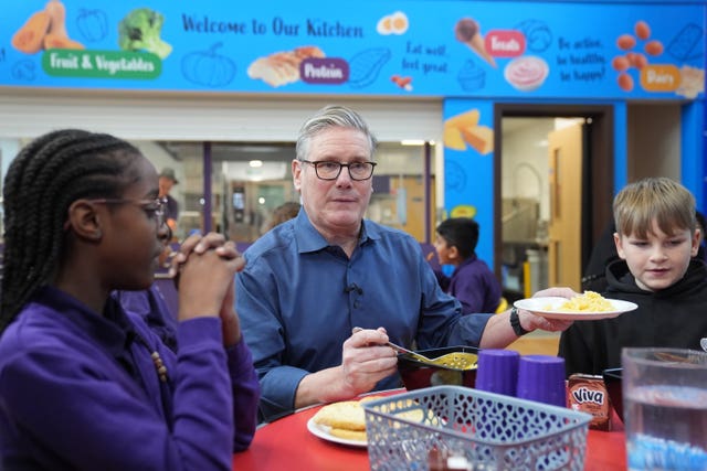 Keir Starmer serving up lunch while sitting at a table with school children