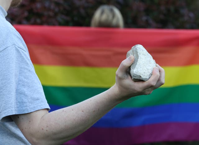 Someone holding a rock in front of a rainbow flag