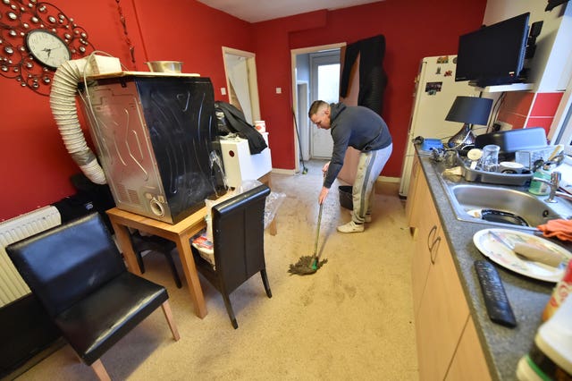 Lee Griffiths mopping the kitchen floor after flooding damaged his house on Rhyd-Yr-Helyg road in Nantgarw (Ben Birchall/PA)
