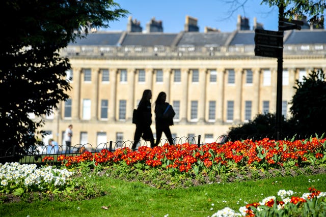 People pass colourful flowers in full bloom near the Royal Crescent, Bath