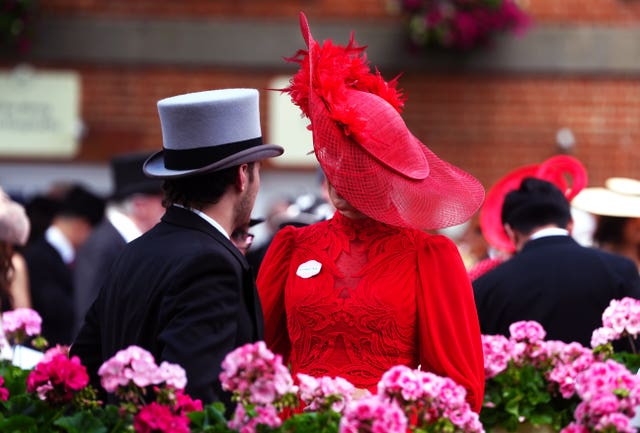 A man in a top hat and a woman in red with a red hat in front of a display of flowers