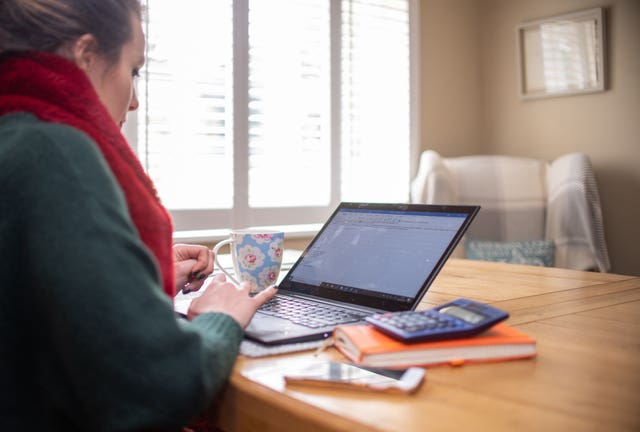 A woman using a laptop on a dining room table set up as a remote office