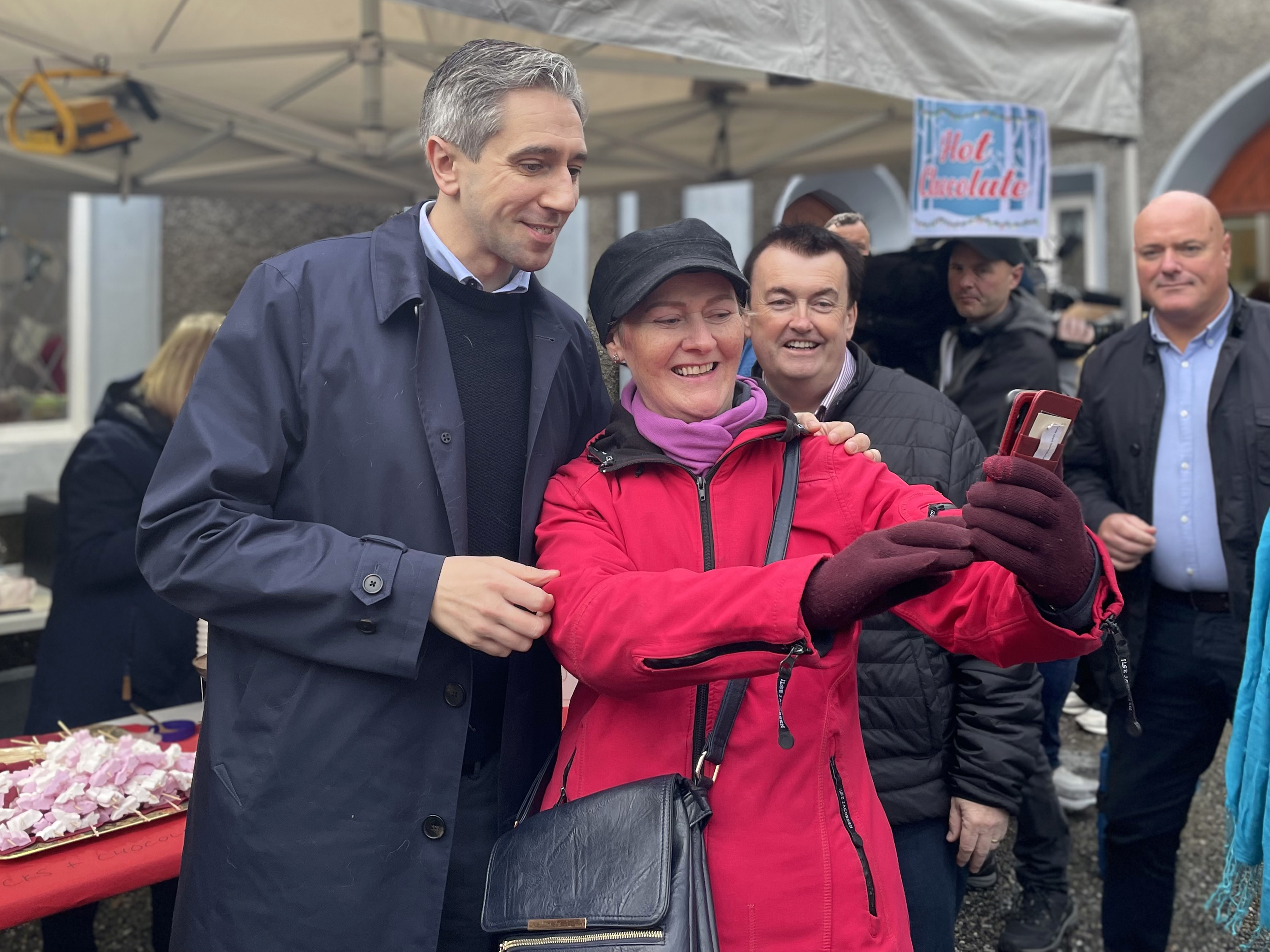 Simon Harris poses for a photo with a member of the public in a cerise jacket