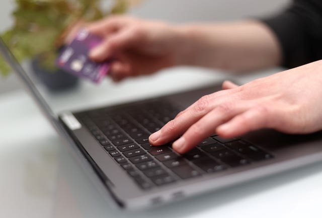 Hands over a laptop keyboard, one typing and the other holding a bank card.