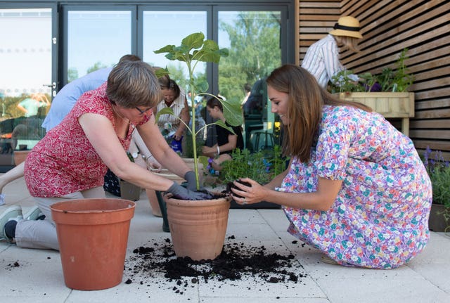 Princess of Wales assists a woman potting plants, with a handful of soil in her hands