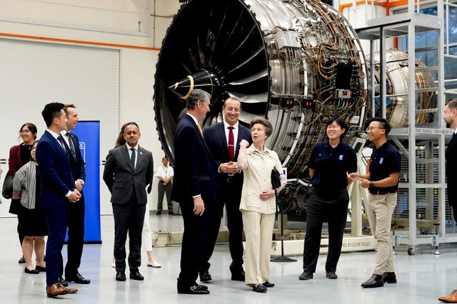 Princess Royal standing among a group of people, with an aeroplane engine behind them