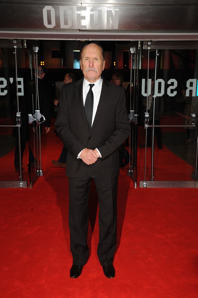 Robert Duvall standing on a red carpet outside the Odeon cinema in Leicester Square, London, wearing a black suit and tie and a white shirt