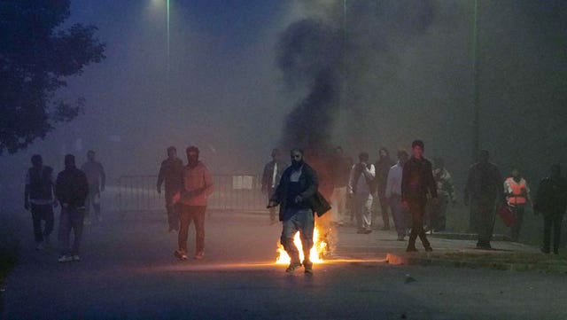A group of people thought to be migrants on a road, with a small fire alight amongst them