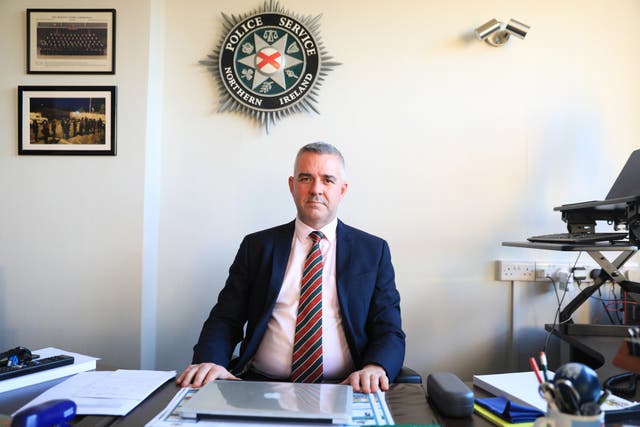 Liam Kelly seated at a desk, with the PSNI logo on the wall behind him