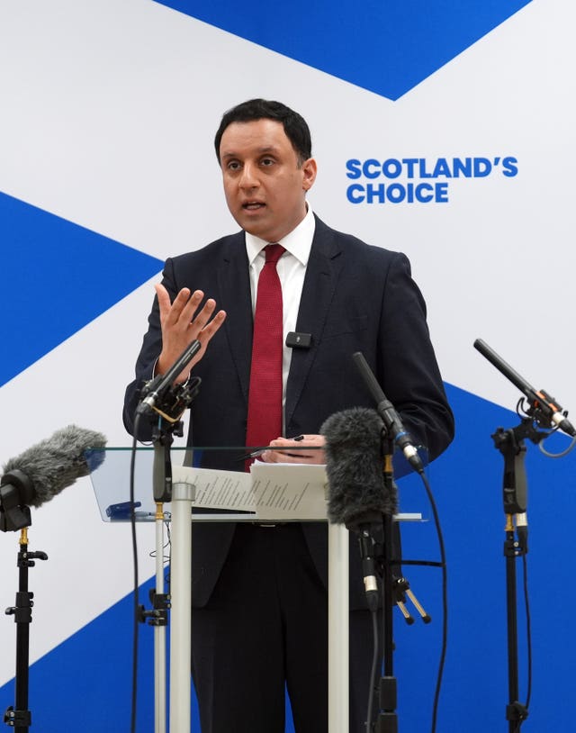 Anas Sarwar speaking from a lectern, in front of a large Scottish flag which has the message 'Scotland's choice' on it