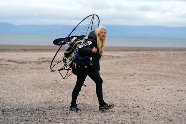 Sacha Dench walking on a beach wearing a paramotor