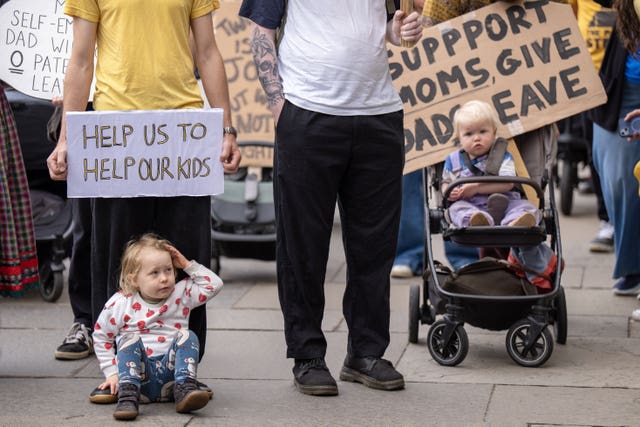A young child sitting on the floor and another in a buggy, alongside their parents during a protest