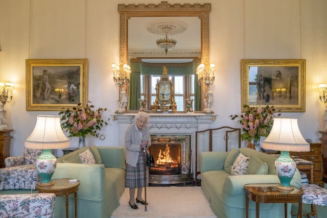 Queen Elizabeth II in her cardigan and tartan skirt, using a walking stick, stands in front of a roaring fire as she waits in the Drawing Room before receiving Liz Truss for an audience at Balmoral Castle, Scotland on September 6 2022