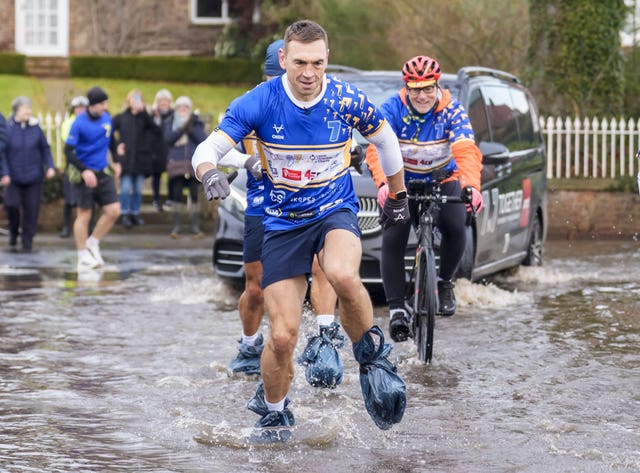 Kevin Sinfield sporting bin bags to cover his footwear as he runs through flood water