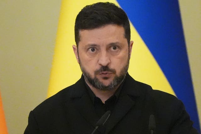 Head and shoulders photo of Volodymyr Zelensky, with the Ukrainian flag behind him