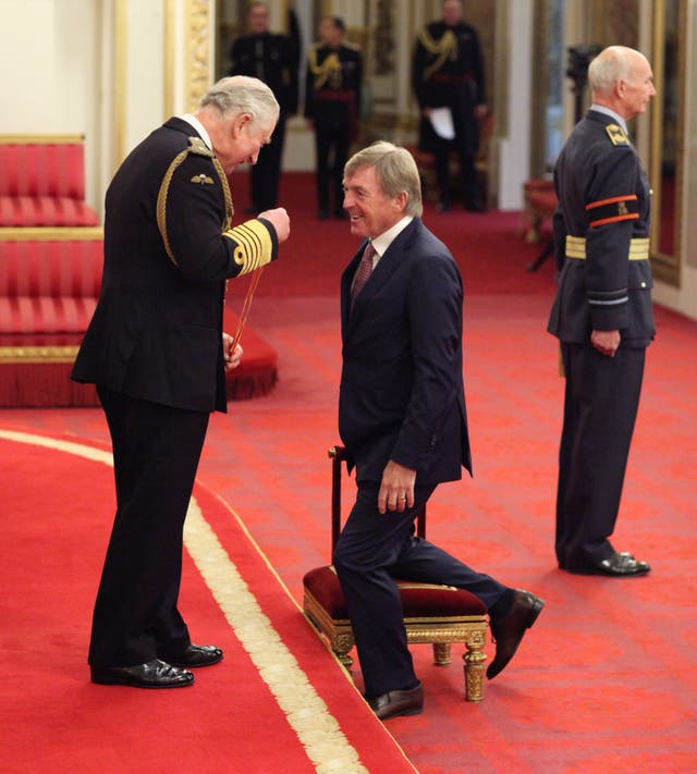 Kenny Dalglish kneels to be knighted by the Prince of Wales at Buckingham Palace.