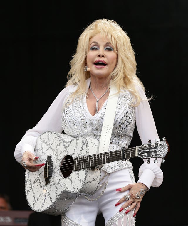 Dolly Parton performing on stage, wearing a silver and white outfit with matching guitar