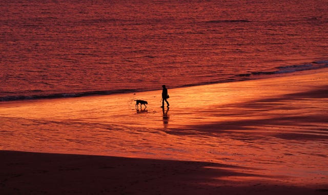 A person walks along Tynemouth Beach as the sun rises in North Shields