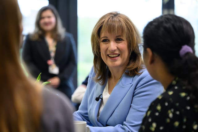 Rachel Reeves smiling, viewed between the backs of two people sitting at a table with her
