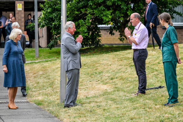 The Prince of Wales remains socially distanced as he a performs a namaste to Professor Mark Pietroni as he arrives with the Duchess of Cornwall at Gloucestershire Royal Hospital