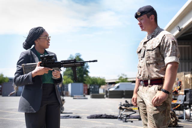 Kemi Badenoch holding a gun while talking to a soldier
