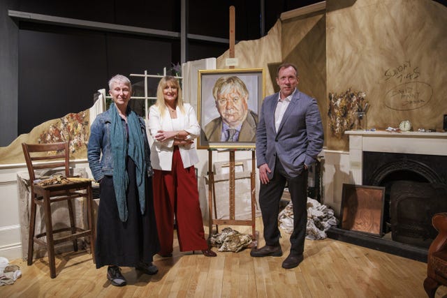 Three people stand beside a portrait