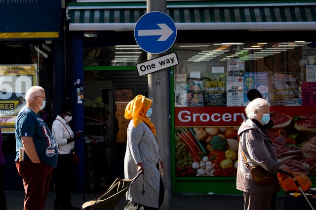 Shoppers wearing face masks observe social distancing as they queue for a shop in east London