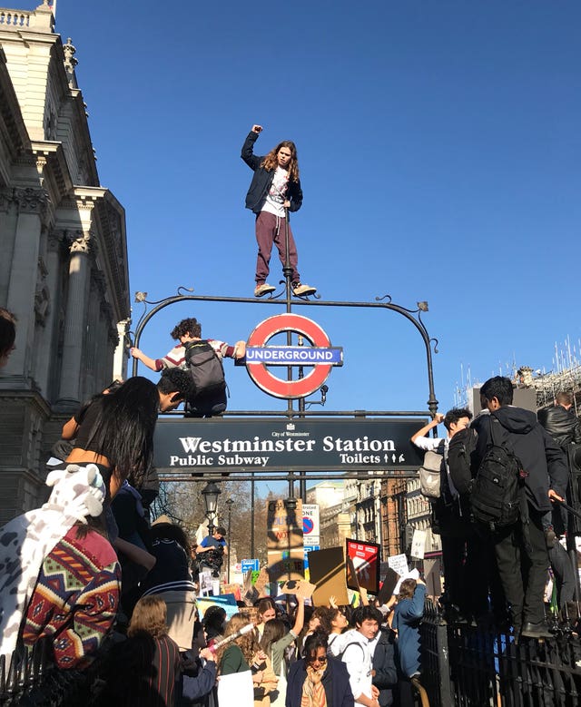 A student from the Youth Strike 4 Climate movement climbs on to an Underground sign during a climate change protest at Parliament Square, Westminster
