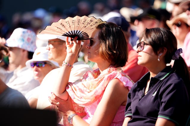 A spectator uses a fan to shield the sun from her eyes