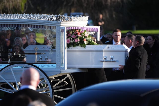 A white coffin is lifted out of a white carriage