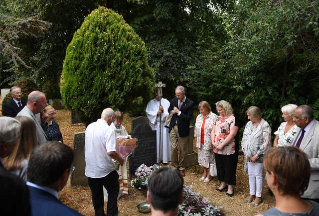 A memorial service is held around the grave of Jean Purdy