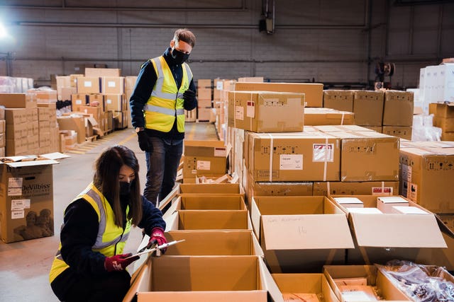 Two people wearing hi-vis vests and protective masks in a room full of cardboard boxes